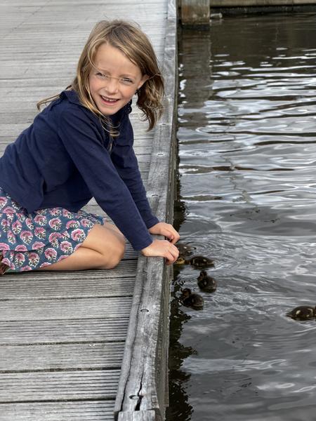 A young girl joyfully interacts with several ducklings from a weathered wooden dock
